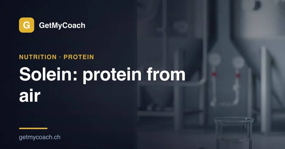 A dish of fine yellow protein powder on a clean light surface with stainless-steel fermentation tanks blurred behind it — cover graphic for the GetMyCoach explainer on Solein, the protein grown from air.