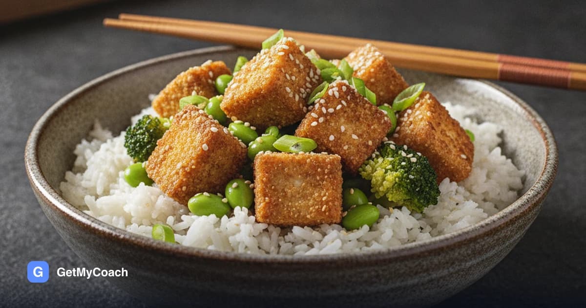 A bowl of rice topped with golden cubes of crispy tofu, bright green edamame and broccoli, scattered with sesame seeds and sliced spring onion.