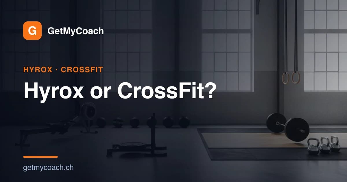 An indoor functional-fitness hall with a loaded sled, wall balls and a rowing machine standing ready under bright light — cover image for the GetMyCoach comparison of Hyrox and CrossFit.
