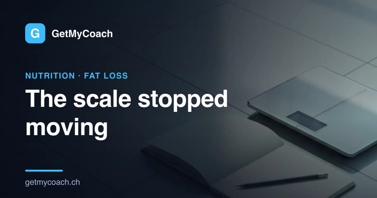 A plain bathroom scale on pale tiles beside an open notebook and a pencil in soft morning light — cover image for the GetMyCoach guide to a stalled scale in a calorie deficit.
