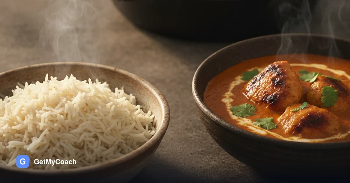A bowl of basmati rice beside a deep orange butter chicken sauce with charred pieces of chicken thigh in it, swirled with cream and scattered with fresh coriander.