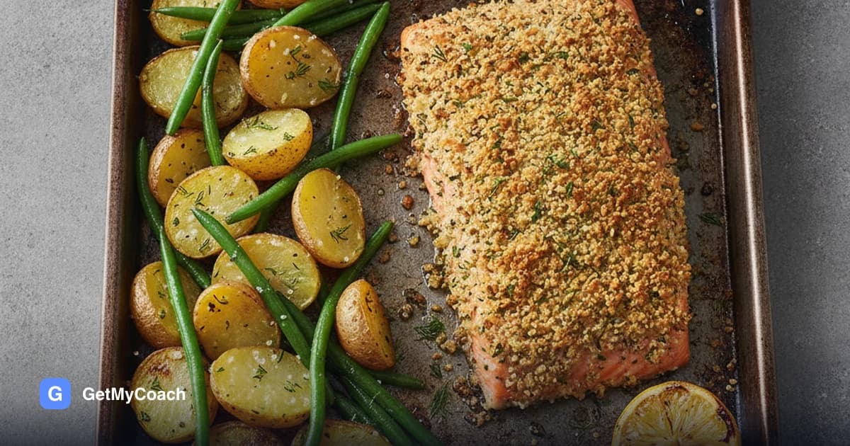 A salmon fillet with a golden herb and breadcrumb crust on a tray beside crushed, crisp-edged new potatoes and bright green beans, with a lemon half alongside.